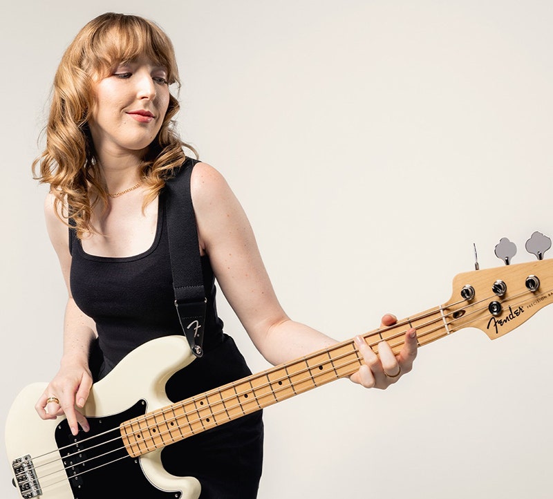 Woman playing a white Fender electric bass guitar against a plain background