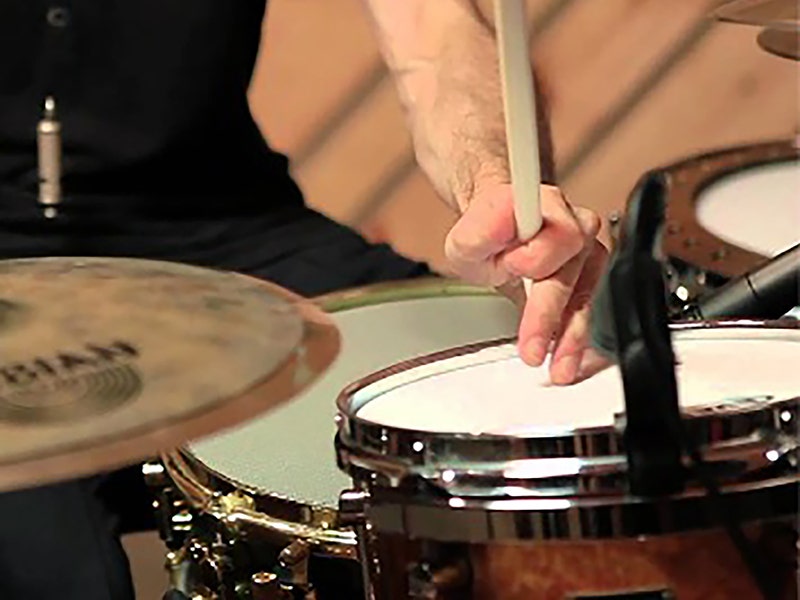 Close-up of a drummer's hands playing a snare drum with drumsticks, with a Zildjian cymbal visible in the foreground