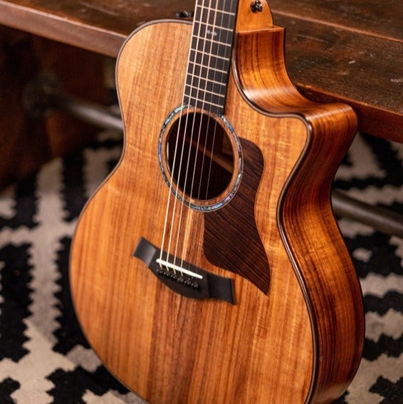 A Taylor acoustic guitar leaning against a bench