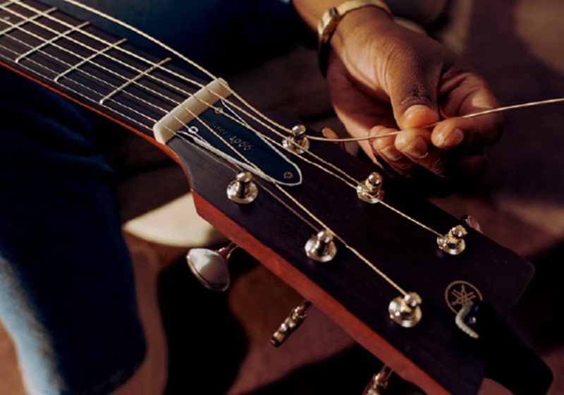 A close-up of someone changing strings on a Yamaha guitar.