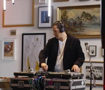 A DJ wearing headphones performs using turntables and a mixer.