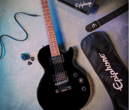 Epiphone Les Paul guitar sitting on a concrete floor with guitar accessories