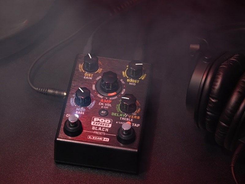 Close-up of a Line 6 POD Go guitar effects pedal surrounded by smoke, with headphones and guitar cables nearby.