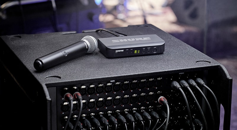 Wireless handheld microphone and receiver resting on top of an audio rack mixer in a live music setup.