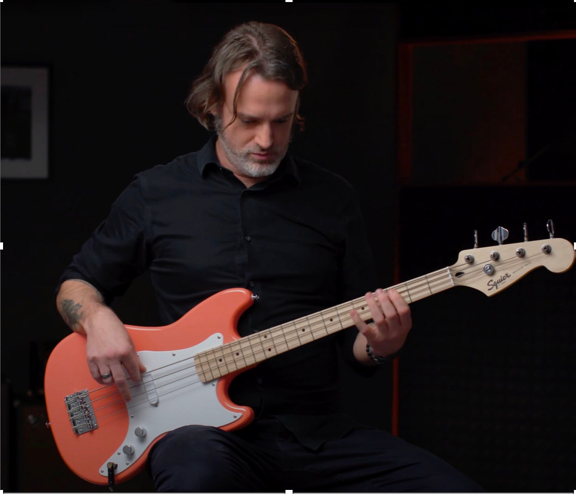 Man playing an orange fender squire bass