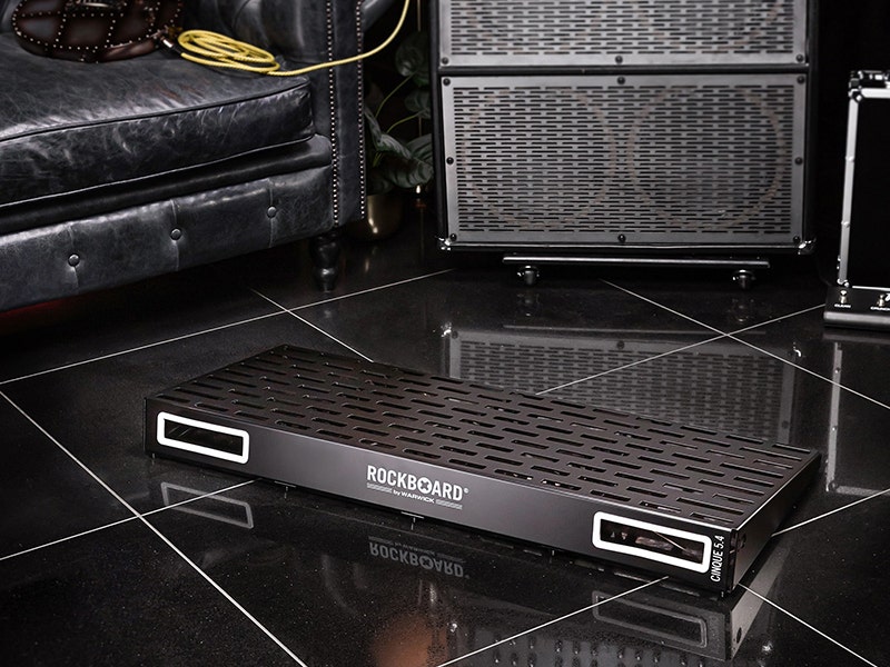 Guitar pedalboard with black metal chassis on a glossy stage floor