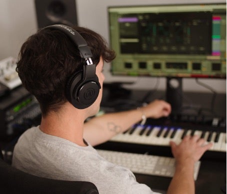 A person wearing Audio-Technica headphones plays a keyboard.