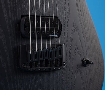 Close up on the strings of a Schecter 7-string guitar on a blue background.