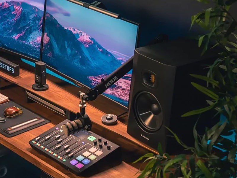 Home studio desk setup with audio mixer, studio monitor speaker, and ultrawide monitor displaying a mountain landscape